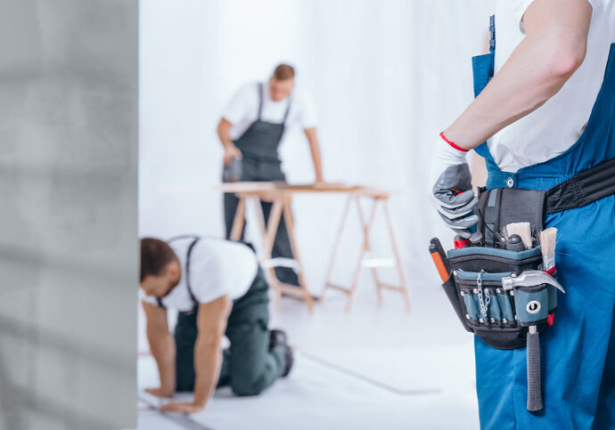 Close-up of handyman with glove on hand and tool belt on blue trousers during home renovation